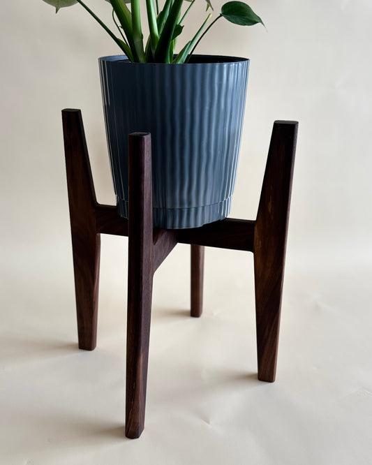 Wooden plant stand with a blue ribbed planter on a plain background