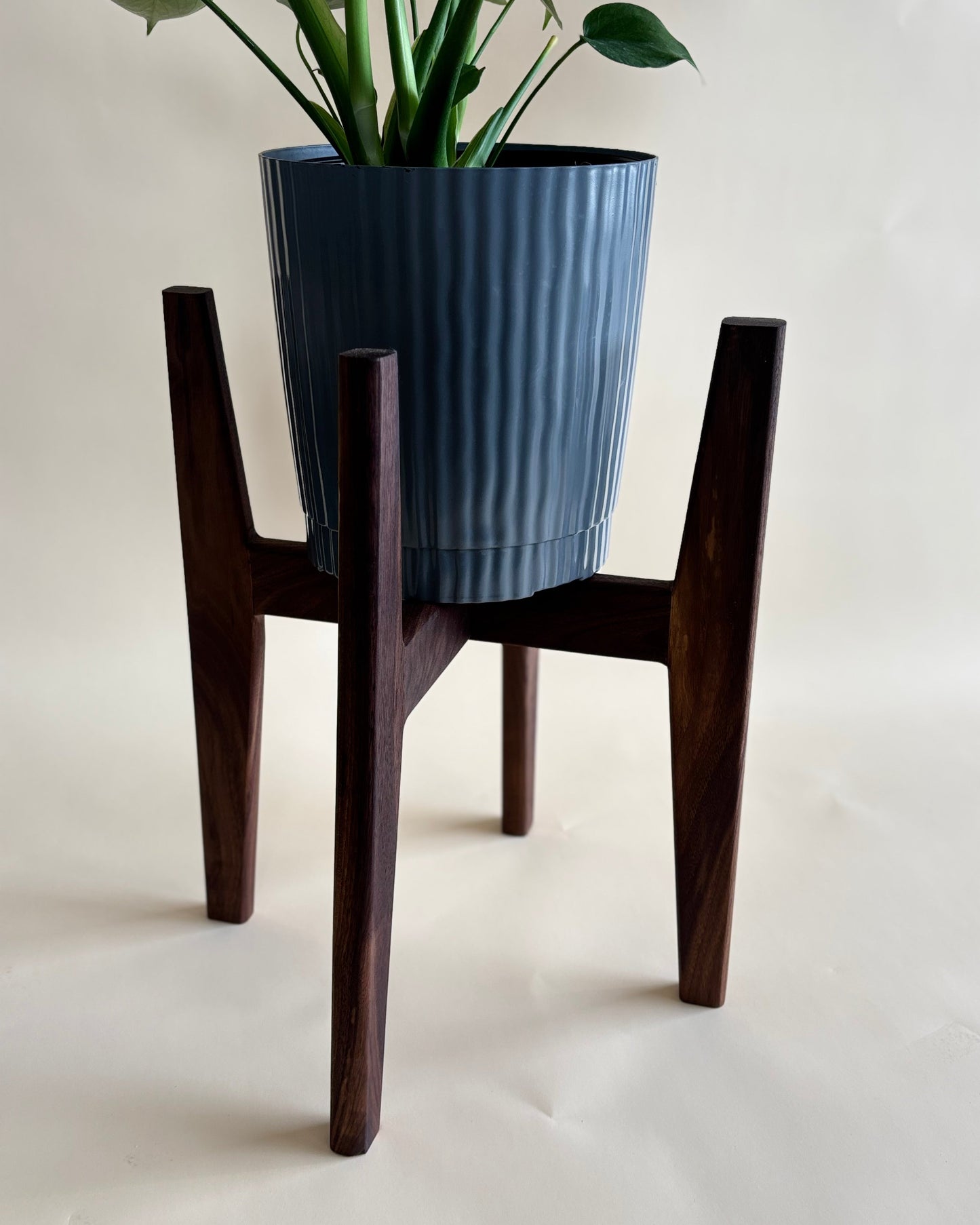 Wooden plant stand with a blue ribbed planter on a plain background